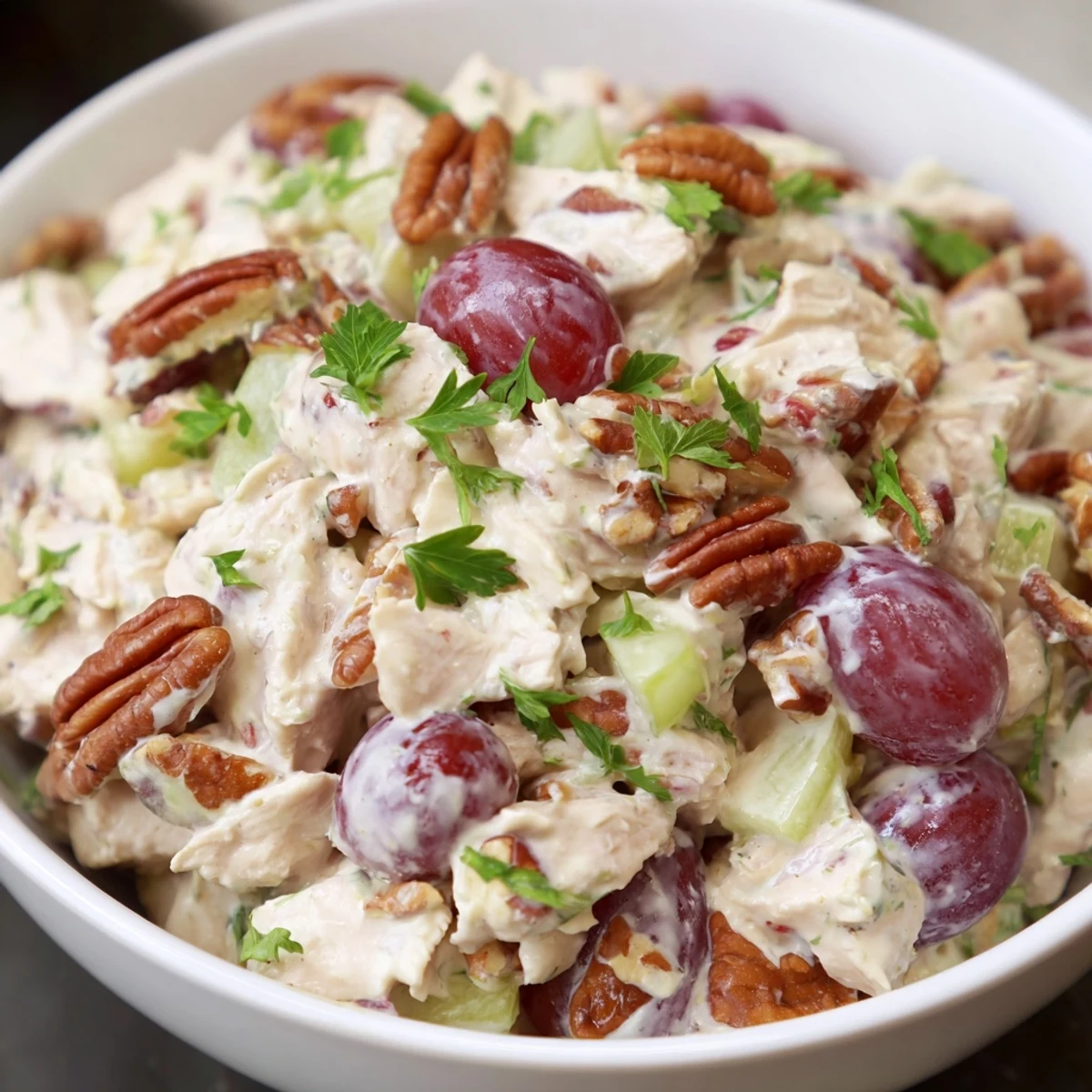 Serving suggestion of Chicken Pecan Salad on a croissant, garnished with fresh parsley and red grapes.