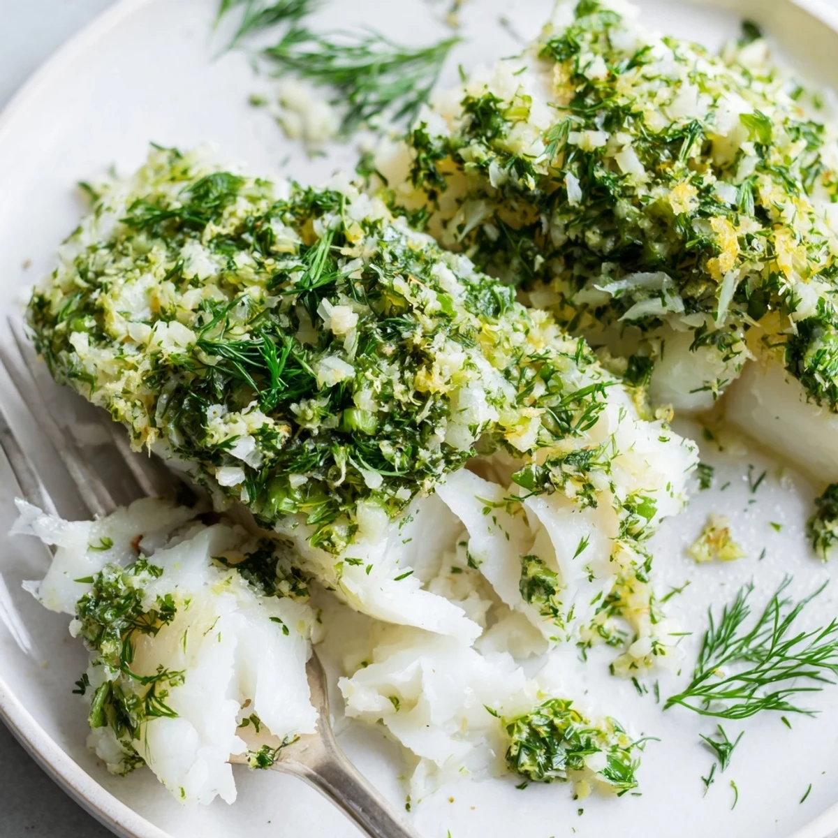Flaky Baked Cod with Herb Butter topped with melted butter and fresh herbs on a white ceramic plate.