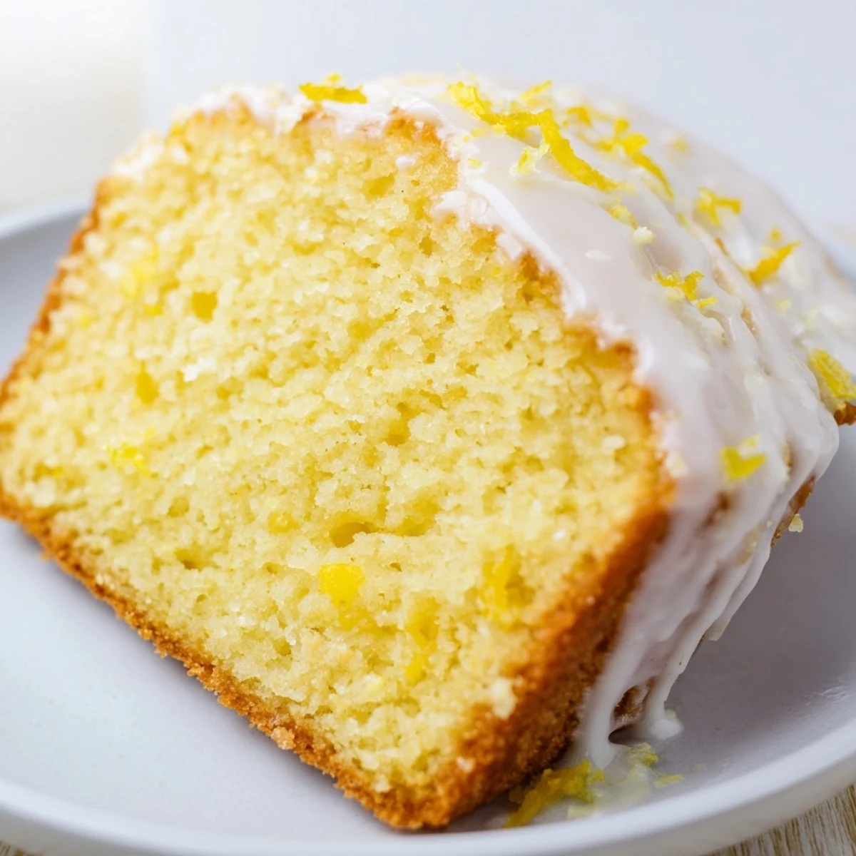 Freshly baked Lemon Loaf Cake with icing cooling on a wire rack, next to sliced lemons. 