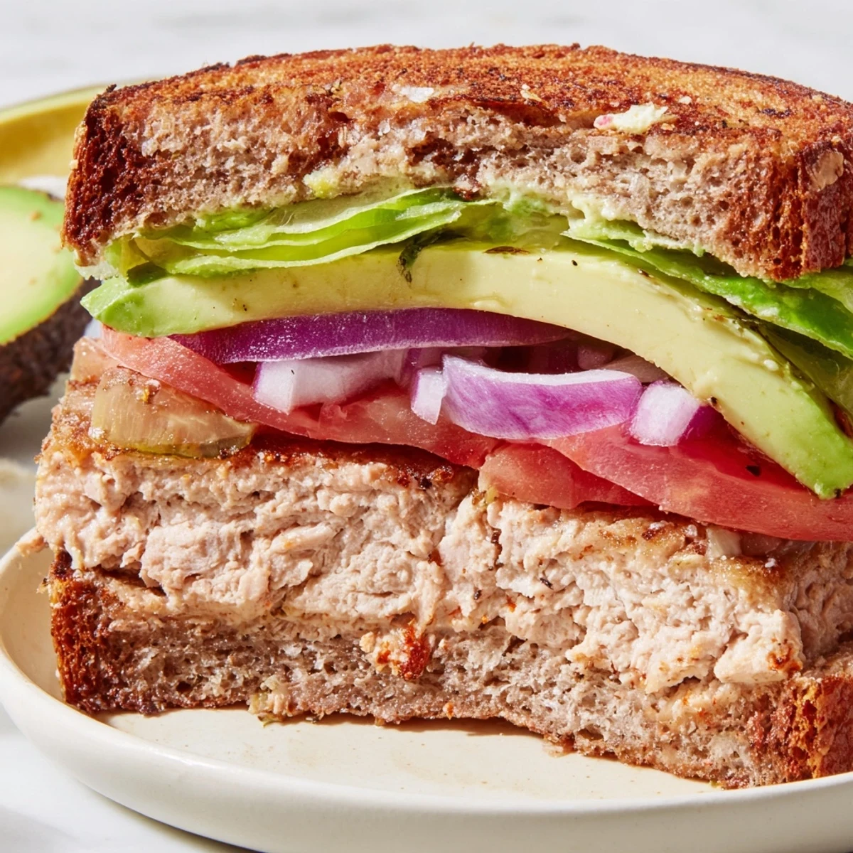 Golden-brown turkey burger with avocado slices on a toasted bun, lettuce, and tomato on a rustic wooden table.