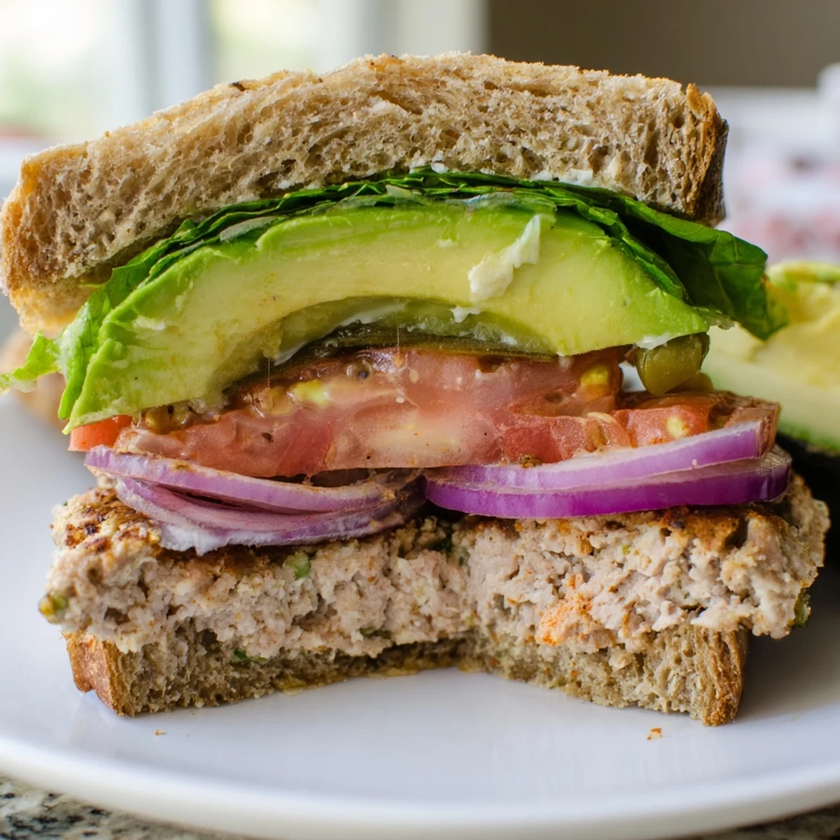 Turkey Burger with Avocado Slices garnished with red onion rings and ketchup, ready to serve alongside sweet potato fries.