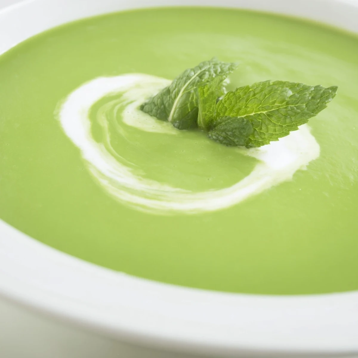 A bowl of vibrant green pea and mint soup garnished with fresh mint leaves, served hot on a rustic table.