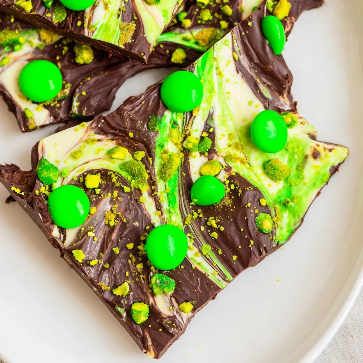 A hand holding a shiny square of St. Patricks Day Mint Chocolate Bark with green candy-coated chocolates glistening.