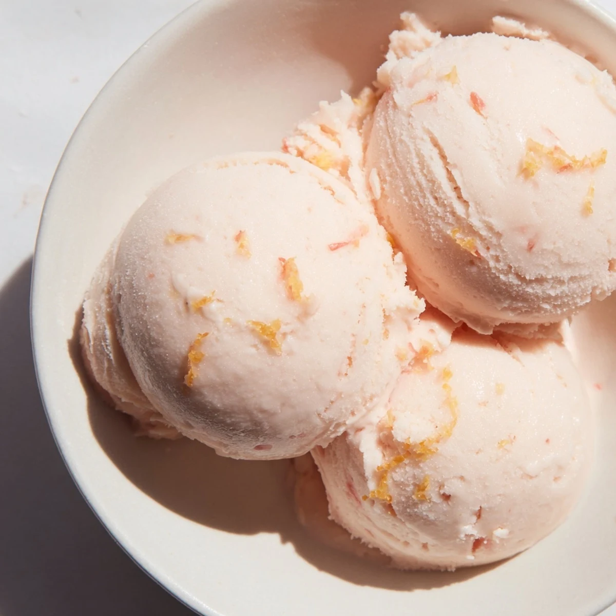 A scoop of Pink Grapefruit Sorbet in a chilled glass, garnished with fresh mint and a curl of zest for a refreshing summer dessert.