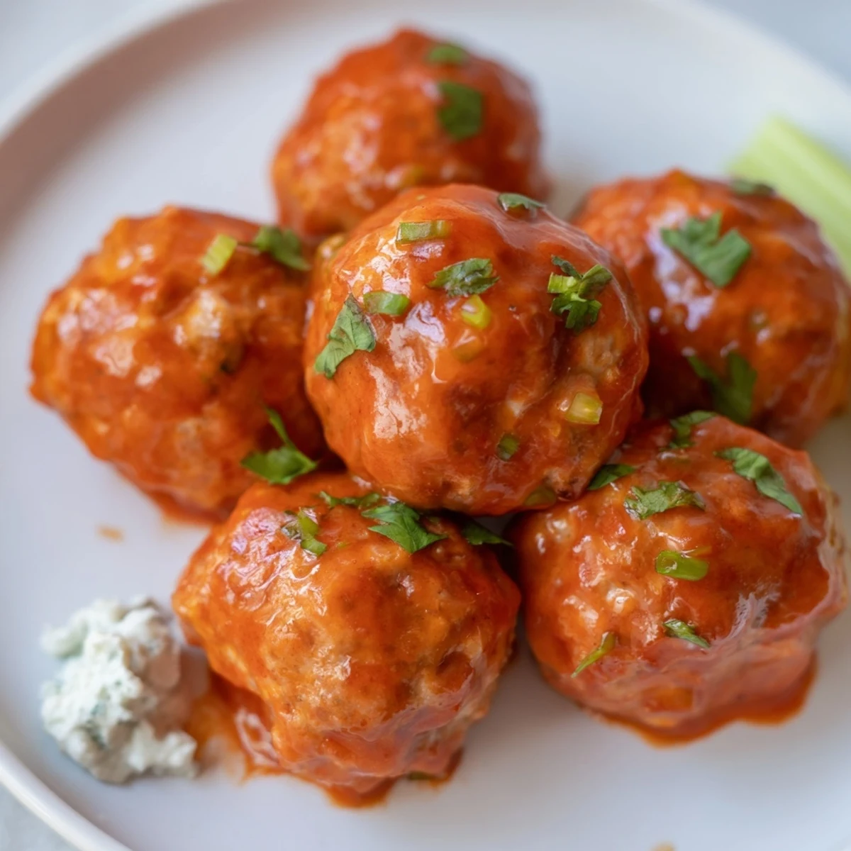 Golden Touchdown Buffalo Chicken Meatballs rest on a baking sheet, their crispy edges glistening under the oven light while a bowl of spicy sauce waits nearby.  