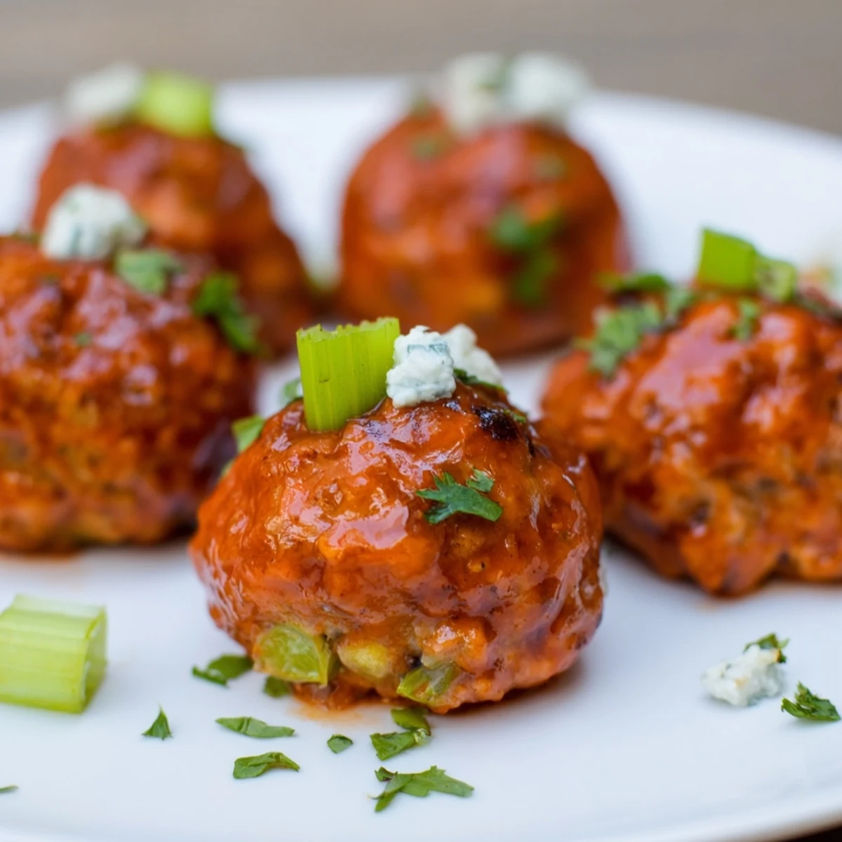 A platter of freshly baked Touchdown Buffalo Chicken Meatballs coated in zesty buffalo sauce, paired with crisp celery sticks and a cool drizzle of ranch dressing.