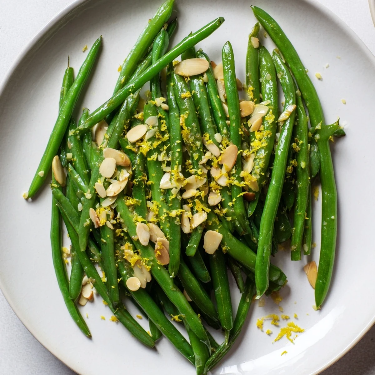 Tender green beans with lemon and almonds on a white platter, ready to serve alongside roasted salmon for dinner.