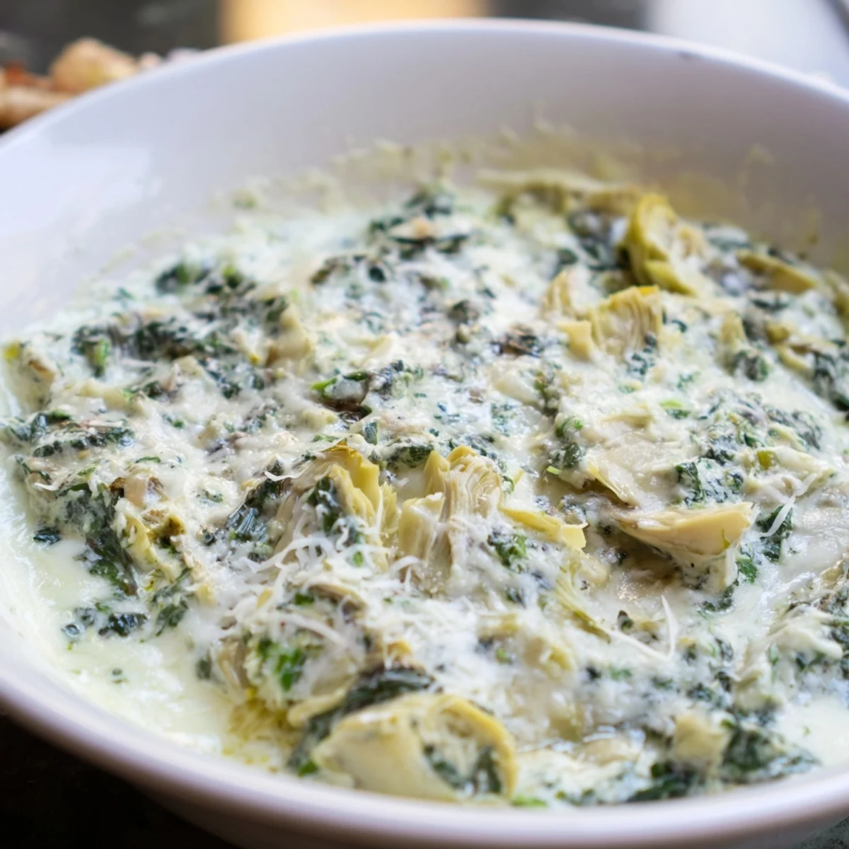 Warm spinach dip with artichokes and gooey cheese, scooped onto a cracker, ready to serve at a gathering.