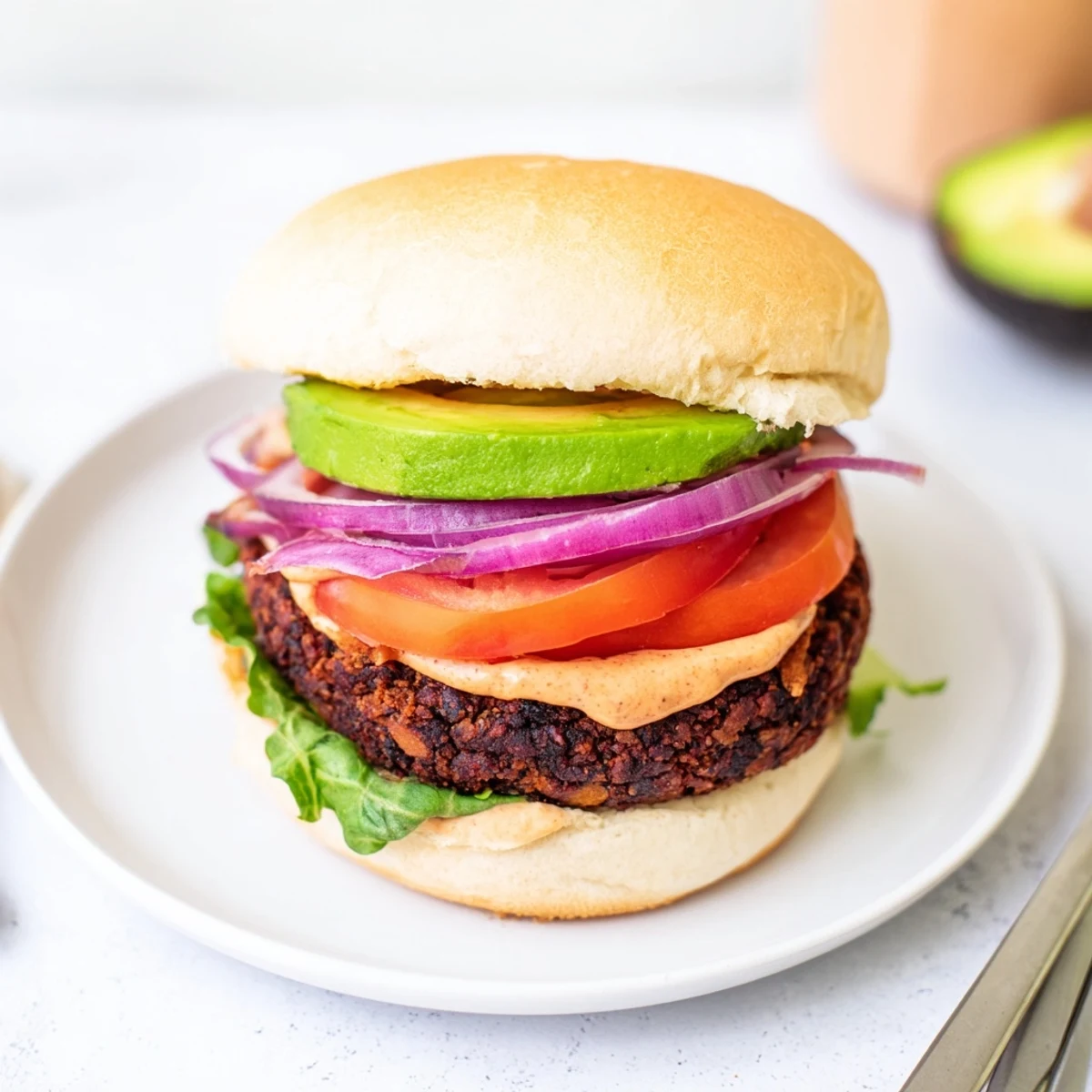 Overhead view of a plated Vegan Black Bean Burger with Chipotle Mayo, featuring vibrant tomato and red onion toppings.
