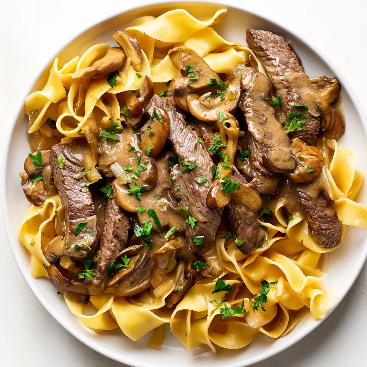 Plated beef stroganoff with egg noodles shows tender beef strips coated in creamy mushroom sauce.