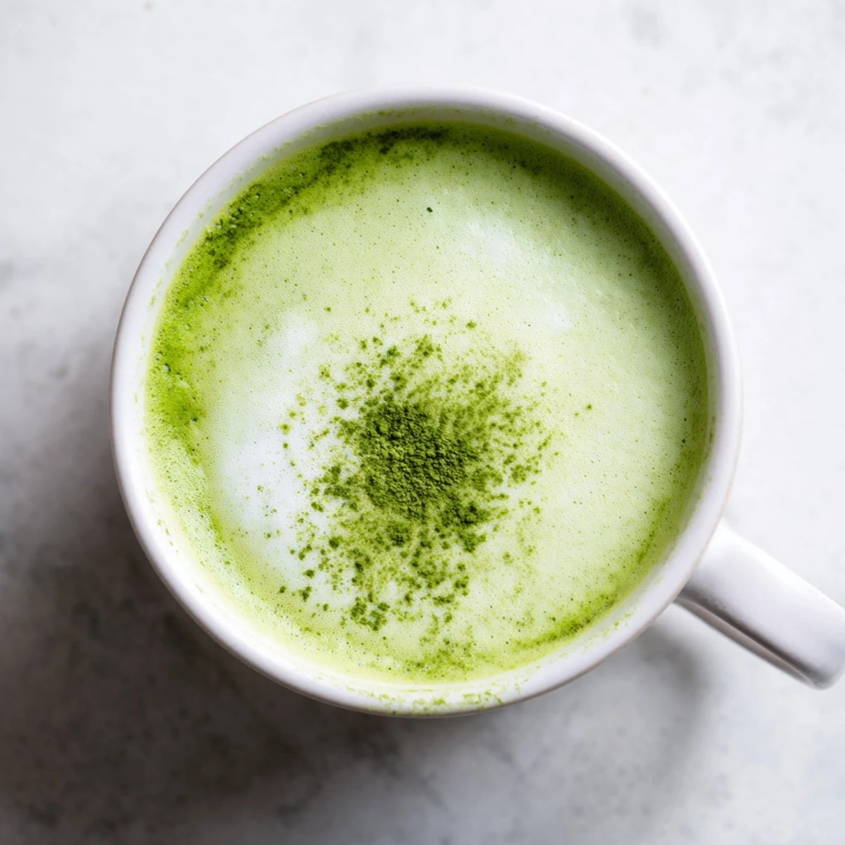 Vibrant green matcha latte with almond milk in a clear glass mug, topped with a delicate froth and dusting of matcha powder.