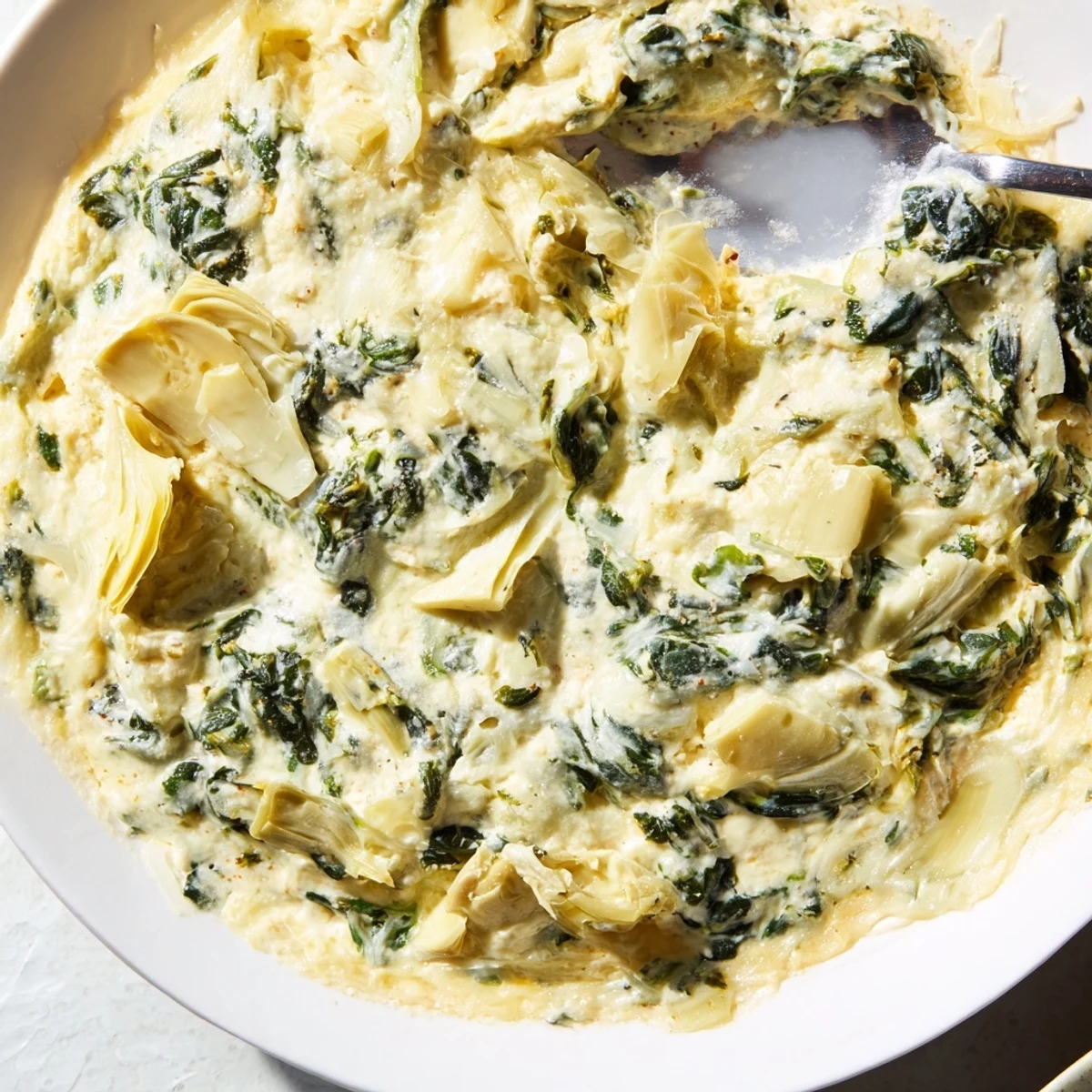 Golden, bubbly Creamy Spinach and Artichoke Dip with Chips served in a white dish, steam rising from the hot cheesy surface.