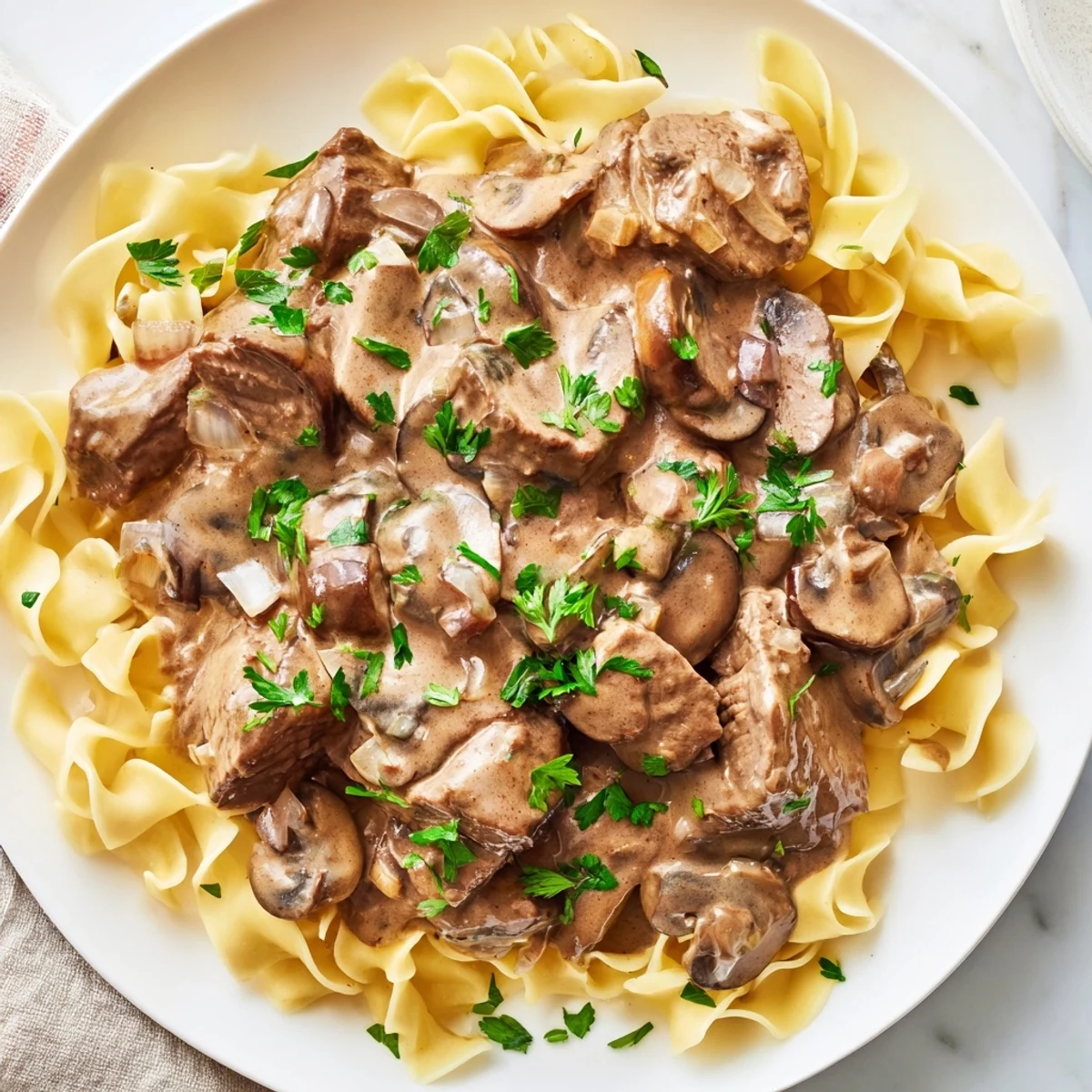 Steaming Beef Stroganoff with Egg Noodles features tender beef strips and creamy mushroom sauce over golden noodles, garnished with fresh parsley.