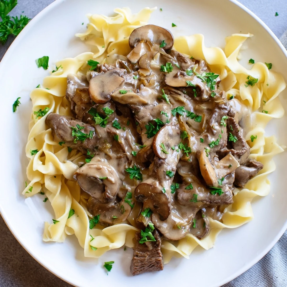 Family-style dinner plate of Beef Stroganoff with Egg Noodles highlights buttery noodles twirled with rich, comforting sauce and a sprinkle of parsley.