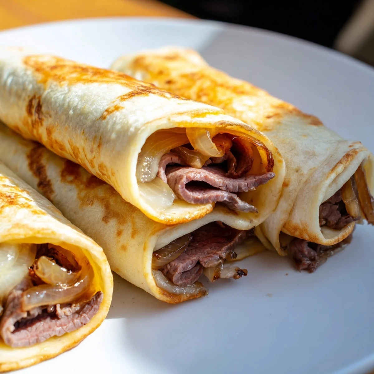 Freshly baked Easy French Dip Tortilla Roll Ups with golden crispy tortillas, melted provolone, and tender roast beef, served with a small bowl of steaming au jus on the side.