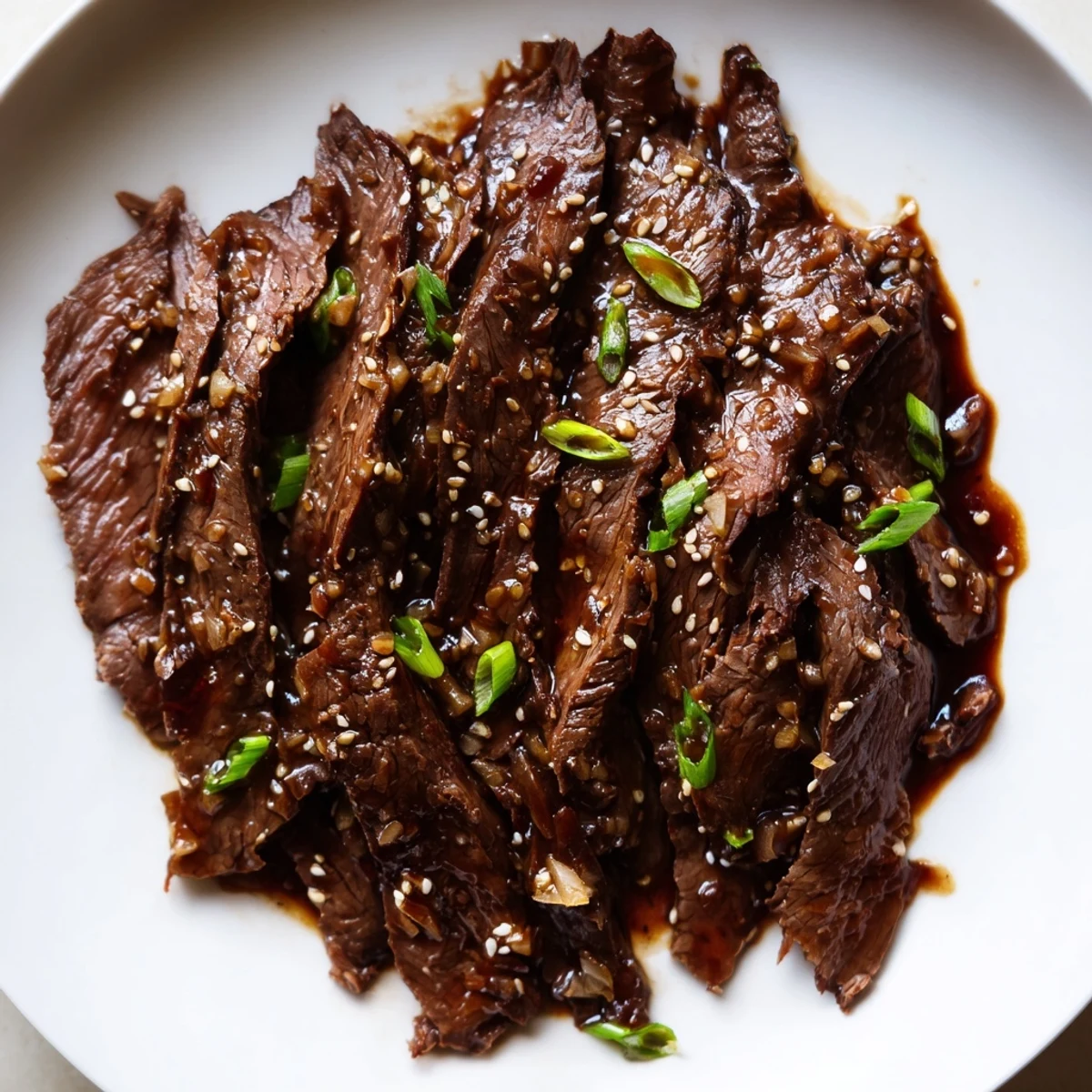 Steaming bowl of Ultimate Slow Cooker Mongolian Beef served over white rice, garnished with green onions and sesame seeds.  
