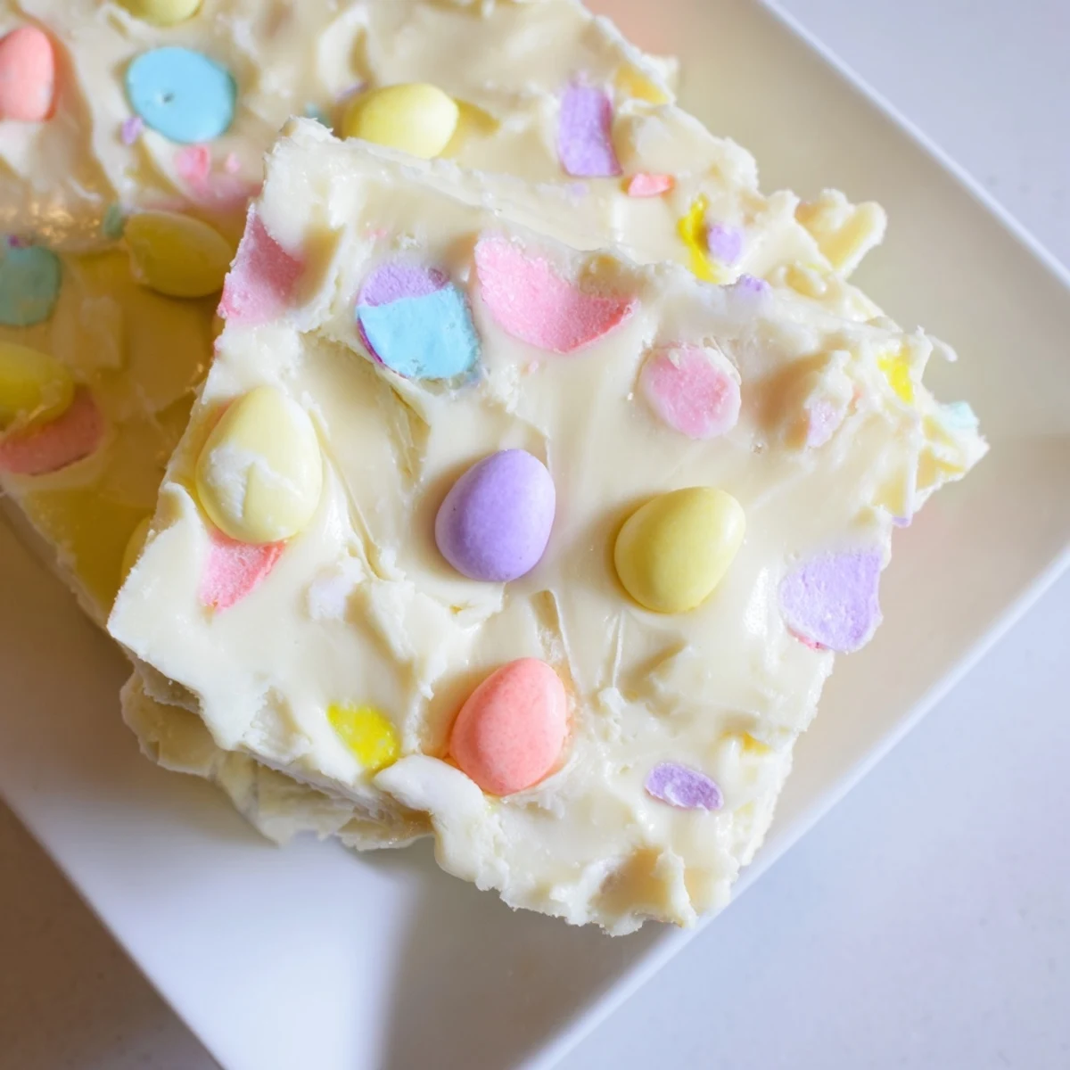 Square cut pieces of Easter Fudge studded with pastel candies displayed on a dessert platter.