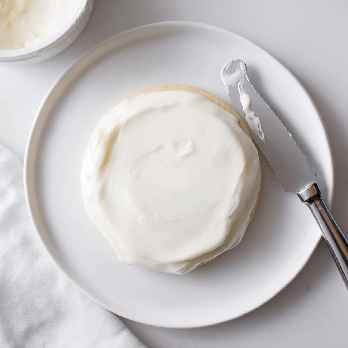 A spoon dips into creamy Easy Sugar Cookie Frosting, swirling glossy white vanilla frosting in a mixing bowl.
