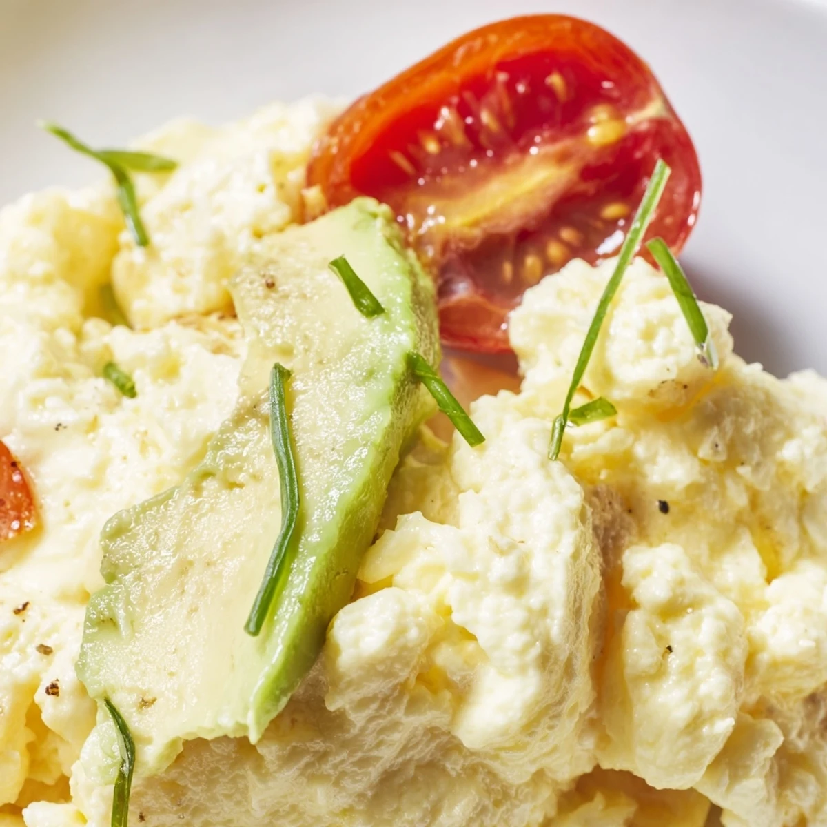 Scrambled Eggs With Avocado Seared Tomato Delight garnished with fresh chives.
