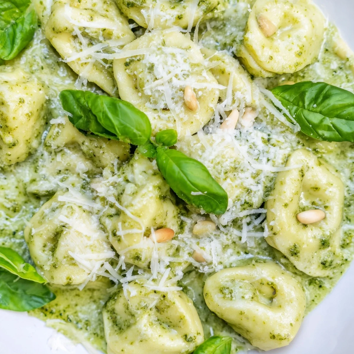 A steaming bowl of Pesto Alfredo Tortellini topped with grated Parmesan and pine nuts.