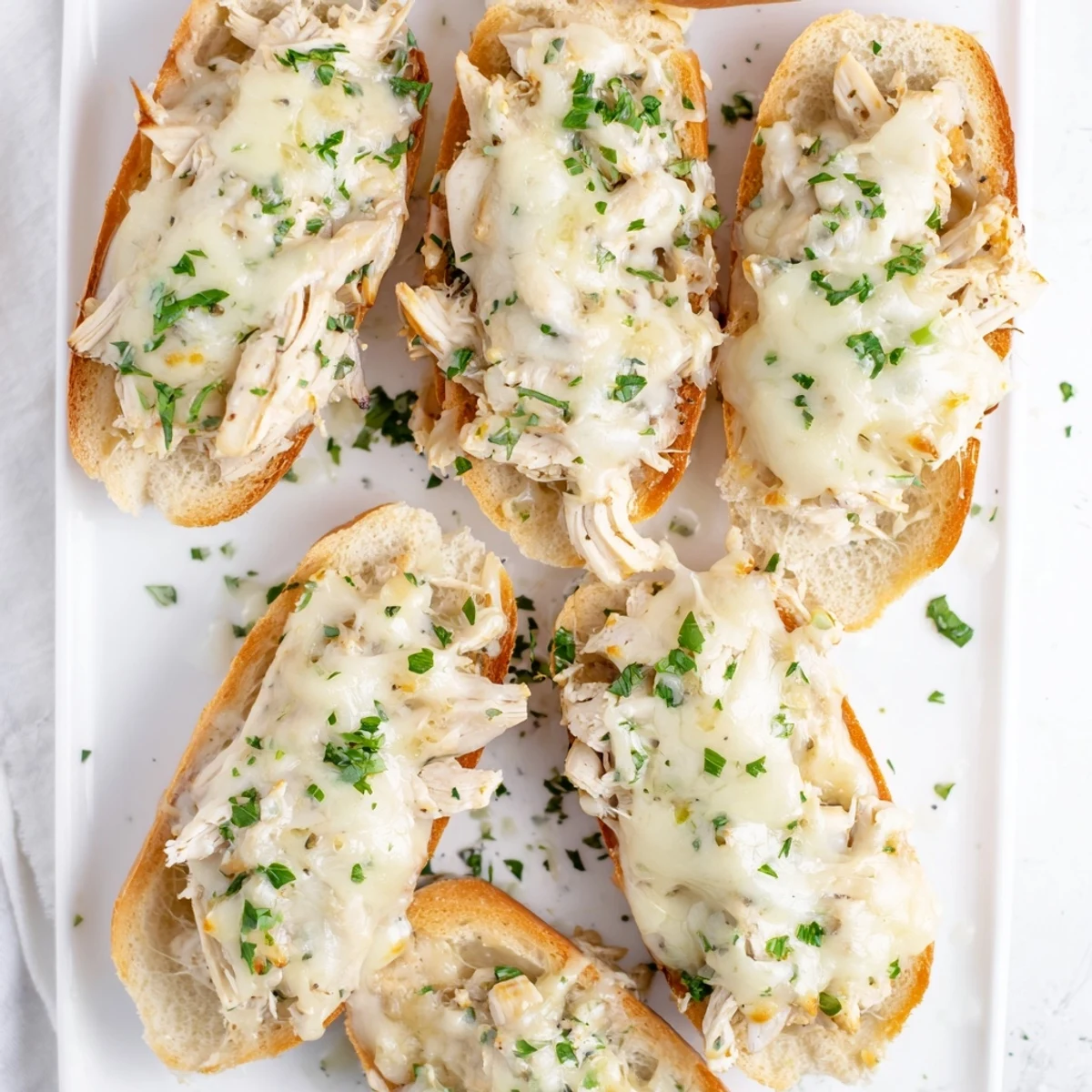 Golden melted cheese and creamy chicken Alfredo topping a buttery garlic bread loaf, ready to serve as a hearty appetizer.