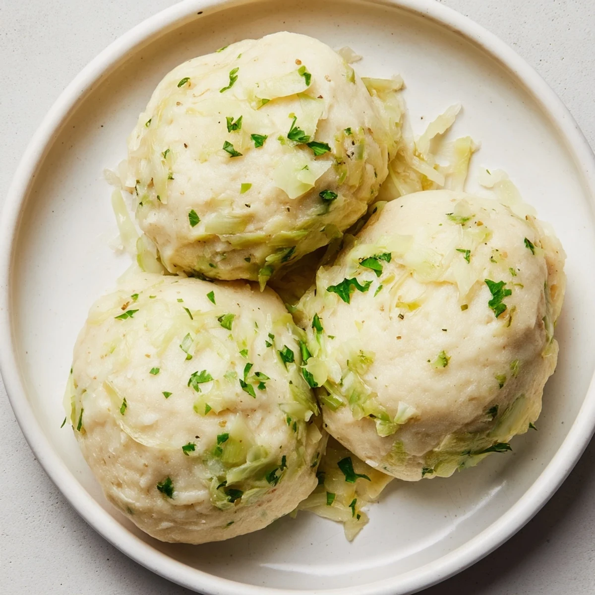 Steamed German Cabbage Dumplings release aromatic nutmeg and parsley in a savory broth, resting beside creamy mushroom sauce.