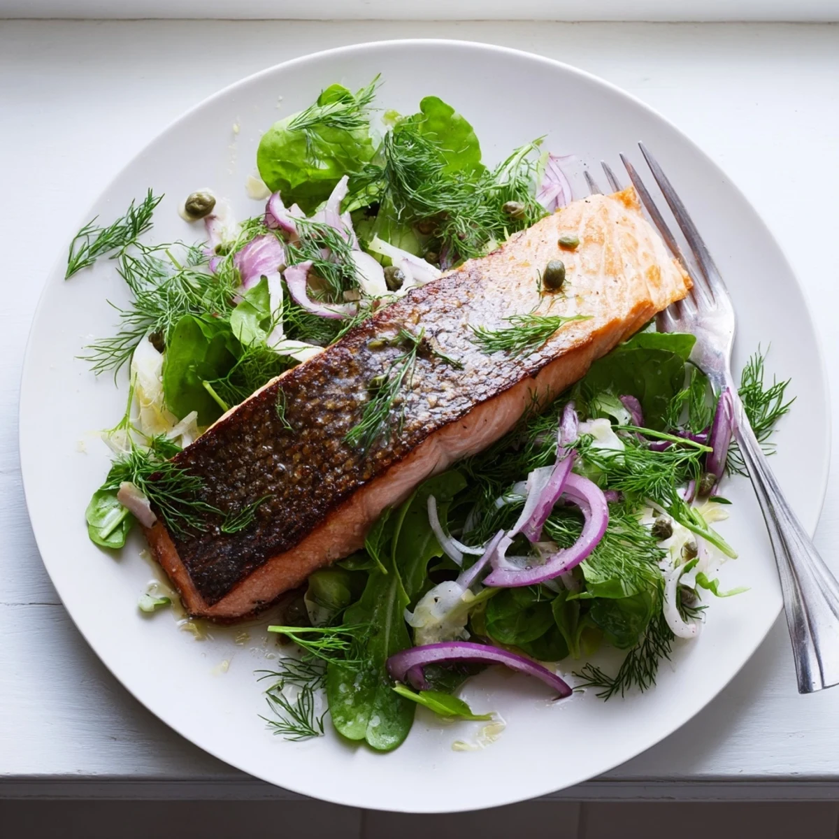 A close up shows Crispy Skin Tasmanian Atlantic Salmon with perfectly seared edges and a fresh lemony herb salad alongside.