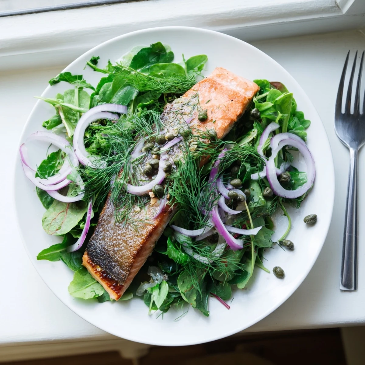 For a vibrant plate, Crispy Skin Tasmanian Atlantic Salmon rests atop mixed greens, red onions, and capers ready to enjoy.