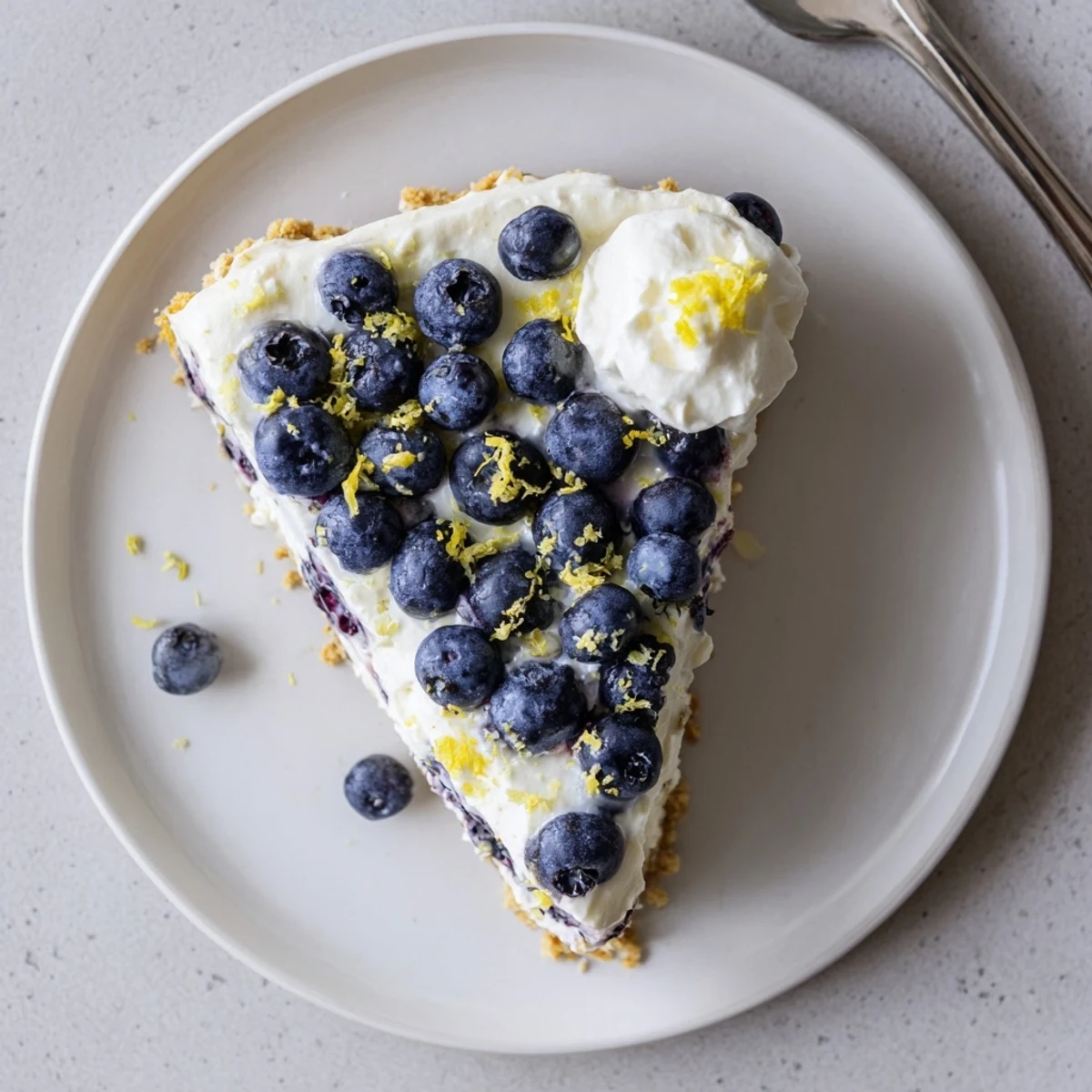 Slice of refreshing lemon blueberry cream cake on a white plate with blueberry garnish
