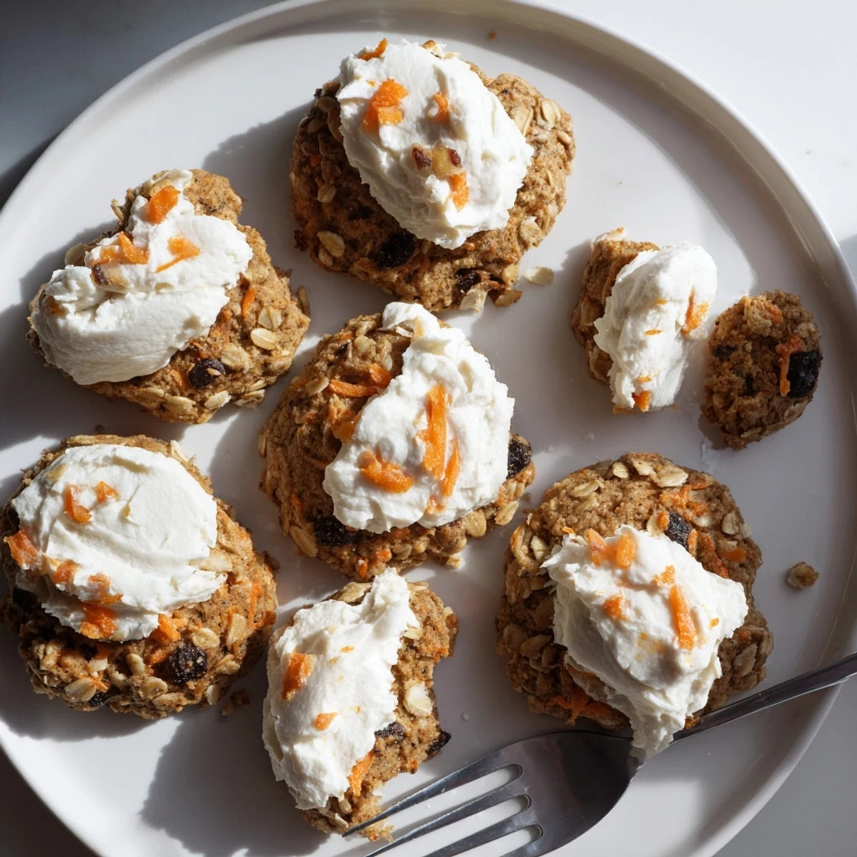 Batch of frosted carrot cake cookies with oats and raisins on a white serving plate
