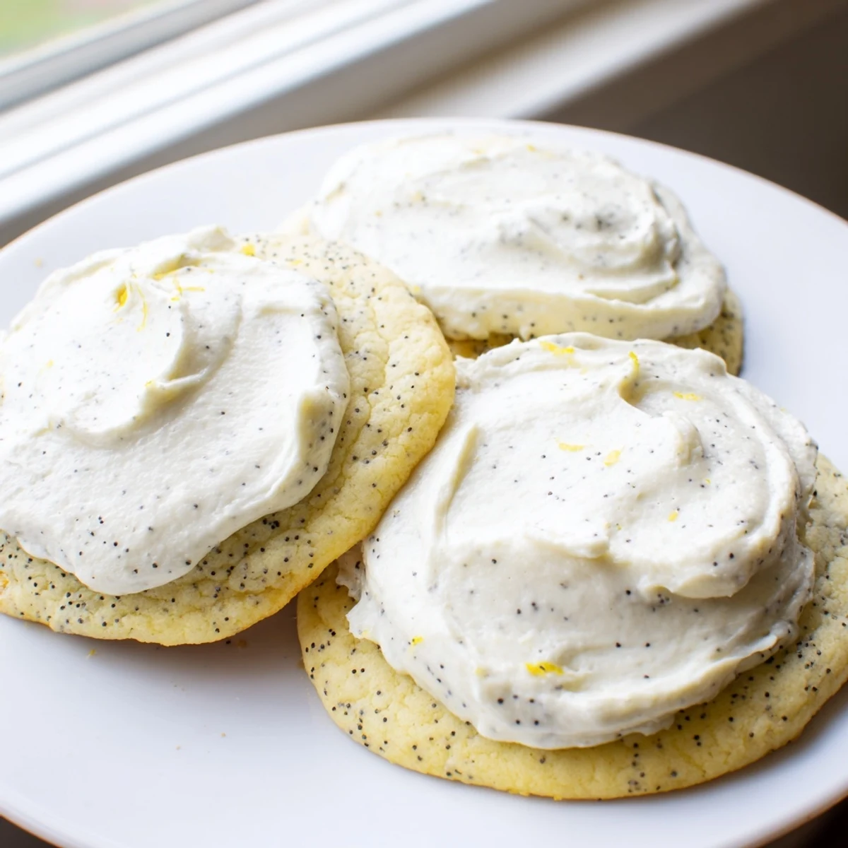 Close up of lemon poppy seed cookies topped with swirls of velvety cheesecake frosting