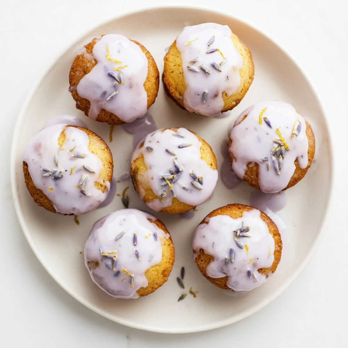 Freshly baked mini lemon cakes with lavender glaze dripping down the fluted sides
