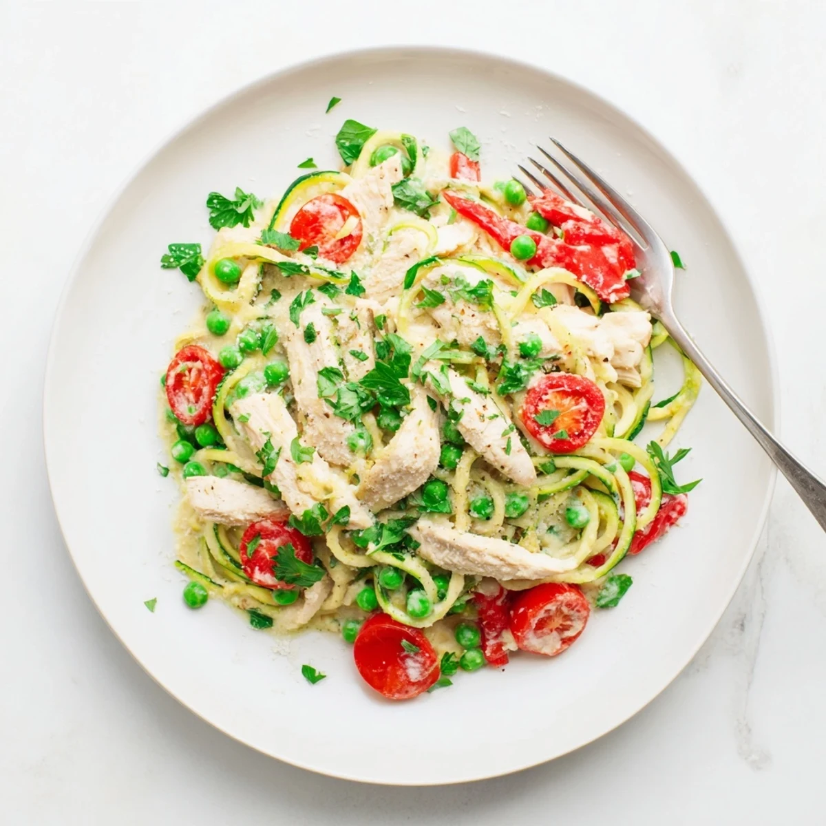 Creamy zucchini noodle chicken Alfredo with colorful vegetables and fresh parsley garnish in a white bowl