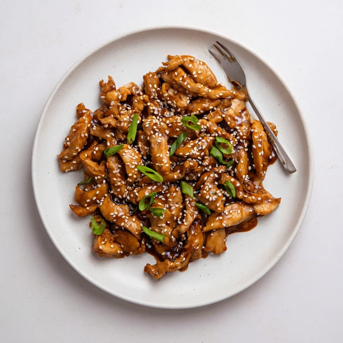 Golden brown Crock Pot Sesame Chicken pieces swimming in a thick sweet and savory glaze, served over steamed white rice in a ceramic serving bowl