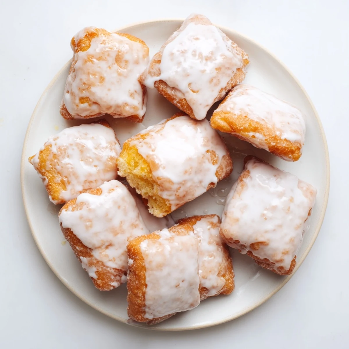 Freshly fried glazed buttermilk beignet squares stacked high with sweet vanilla icing dripping down the sides