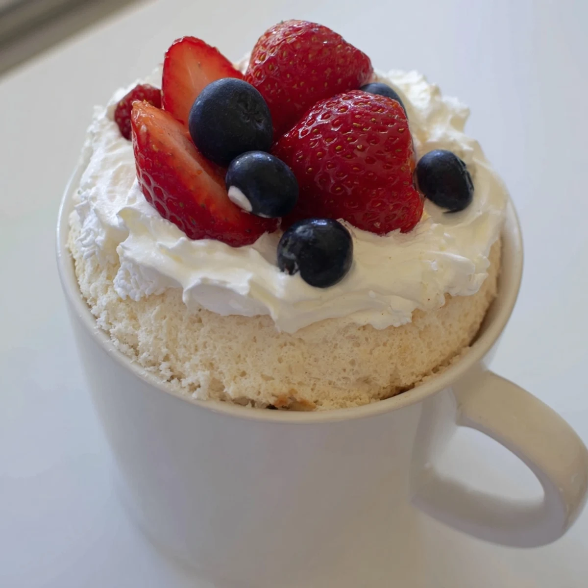 Fluffy angel food cake with whipped cream and fresh berries in a white mug