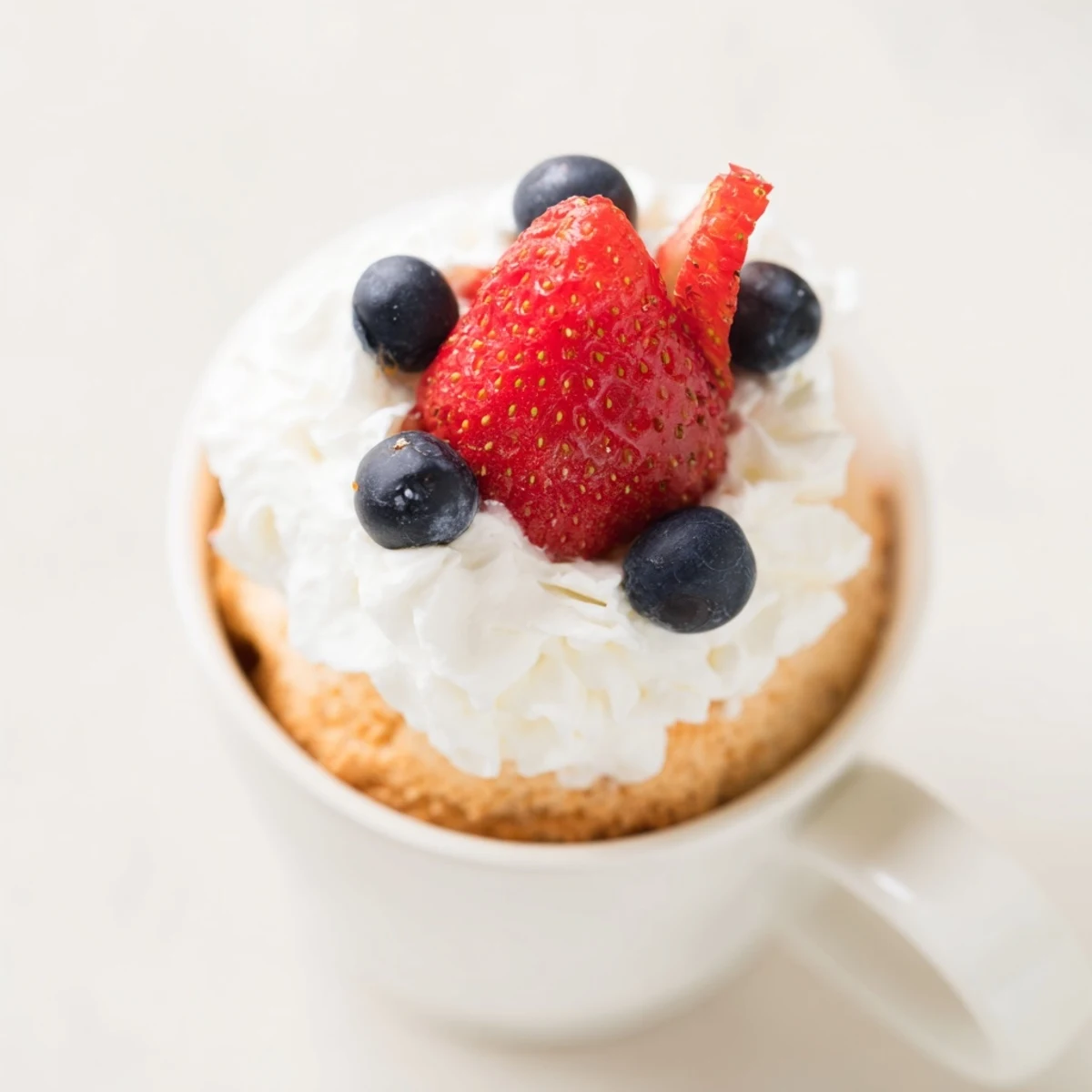 Golden brown air fryer angel food cake mug topped with red strawberries and blueberries