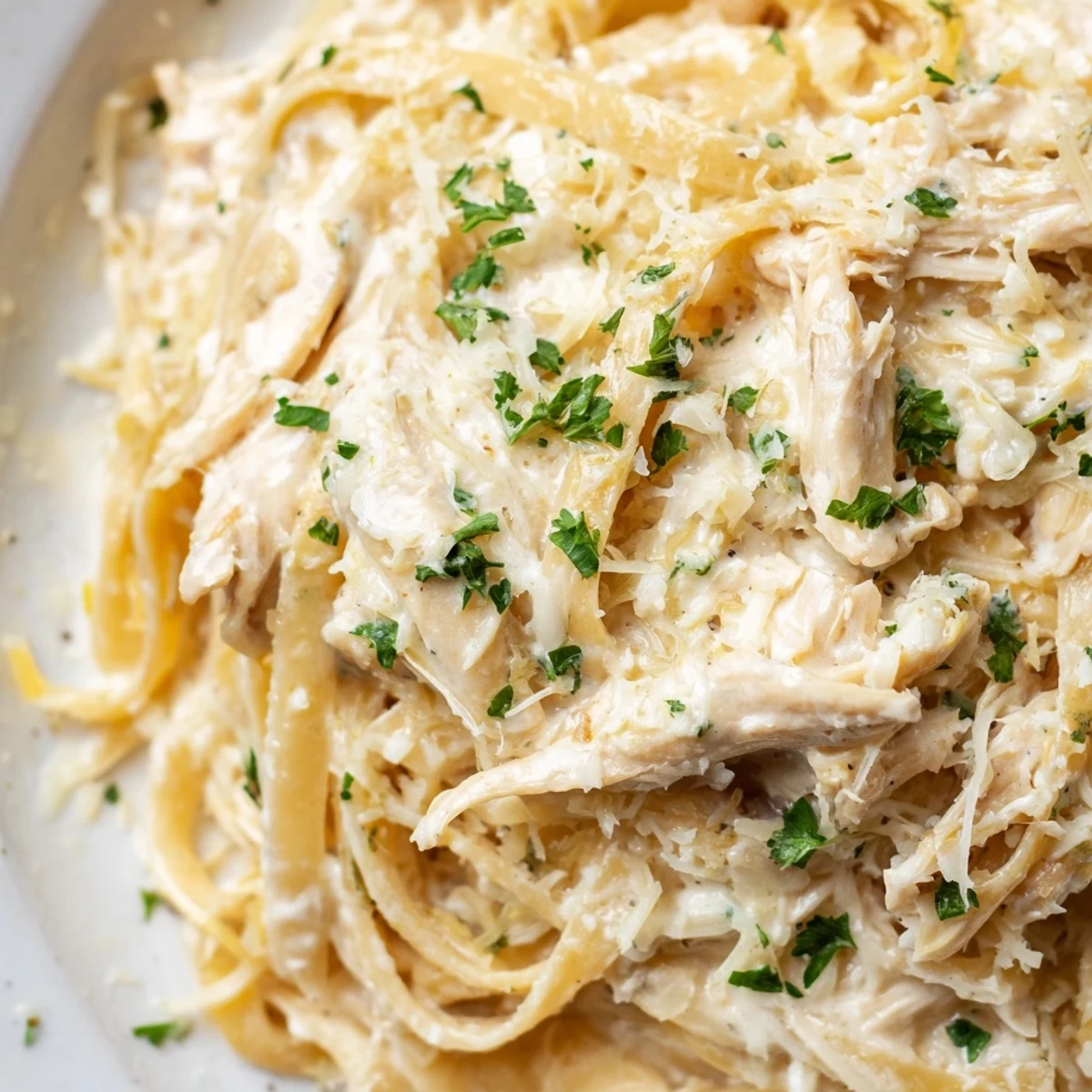 Slow cooker Chicken Alfredo featuring rich parmesan sauce coating perfectly cooked noodles and chicken