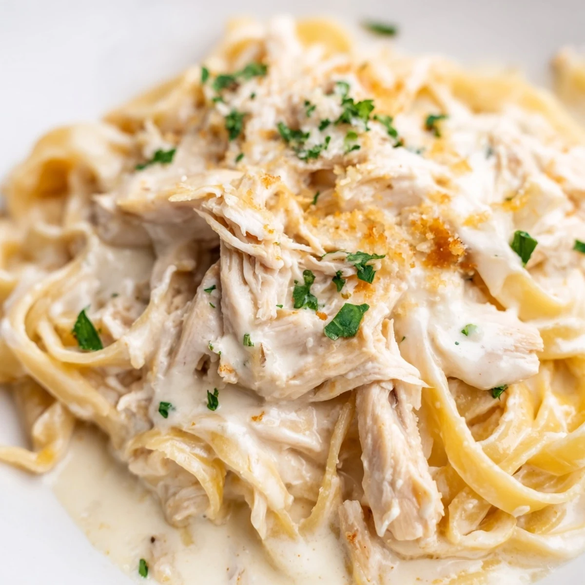Golden chicken Alfredo recipe served in a white bowl garnished with fresh green parsley
