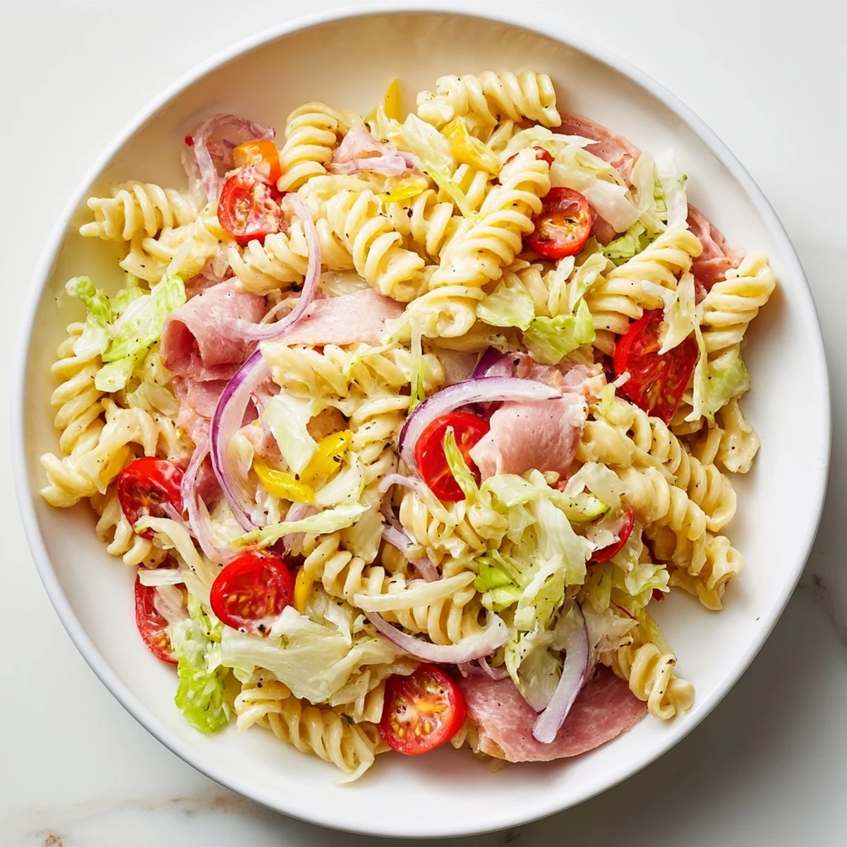 Colorful grinder pasta salad bowl featuring rotini with salami, provolone, cherry tomatoes, and crisp red onions
