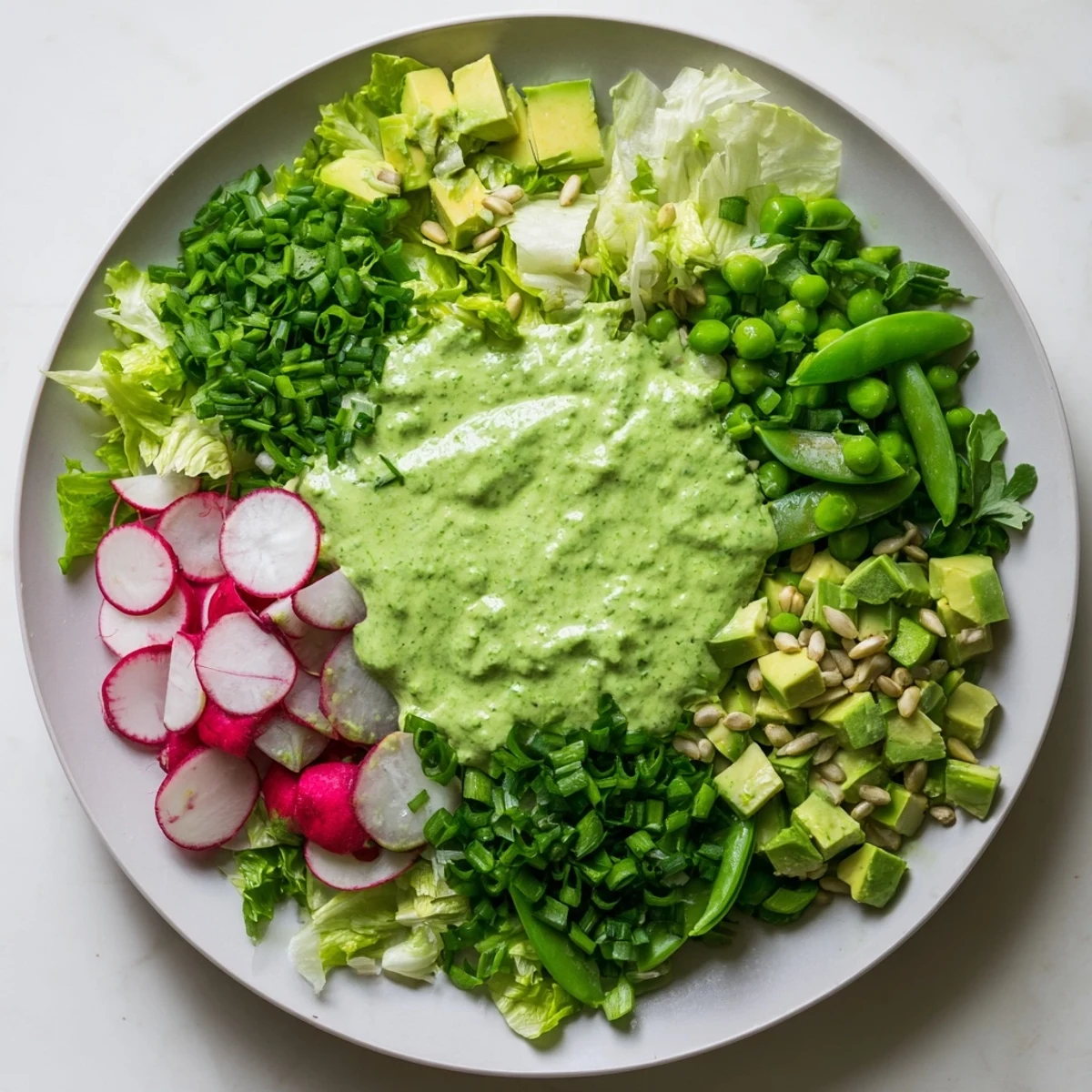 Rustic wooden table topped with Fresh Green Goddess Salad featuring diced cucumber, snap peas, radishes, and creamy green dressing