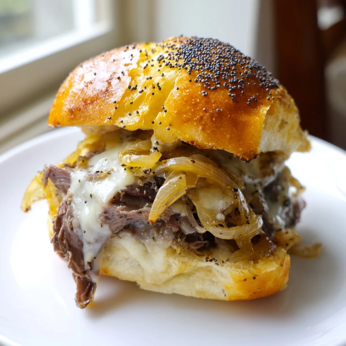 Golden French dip sliders stacked with roast beef and caramelized onions on a baking sheet