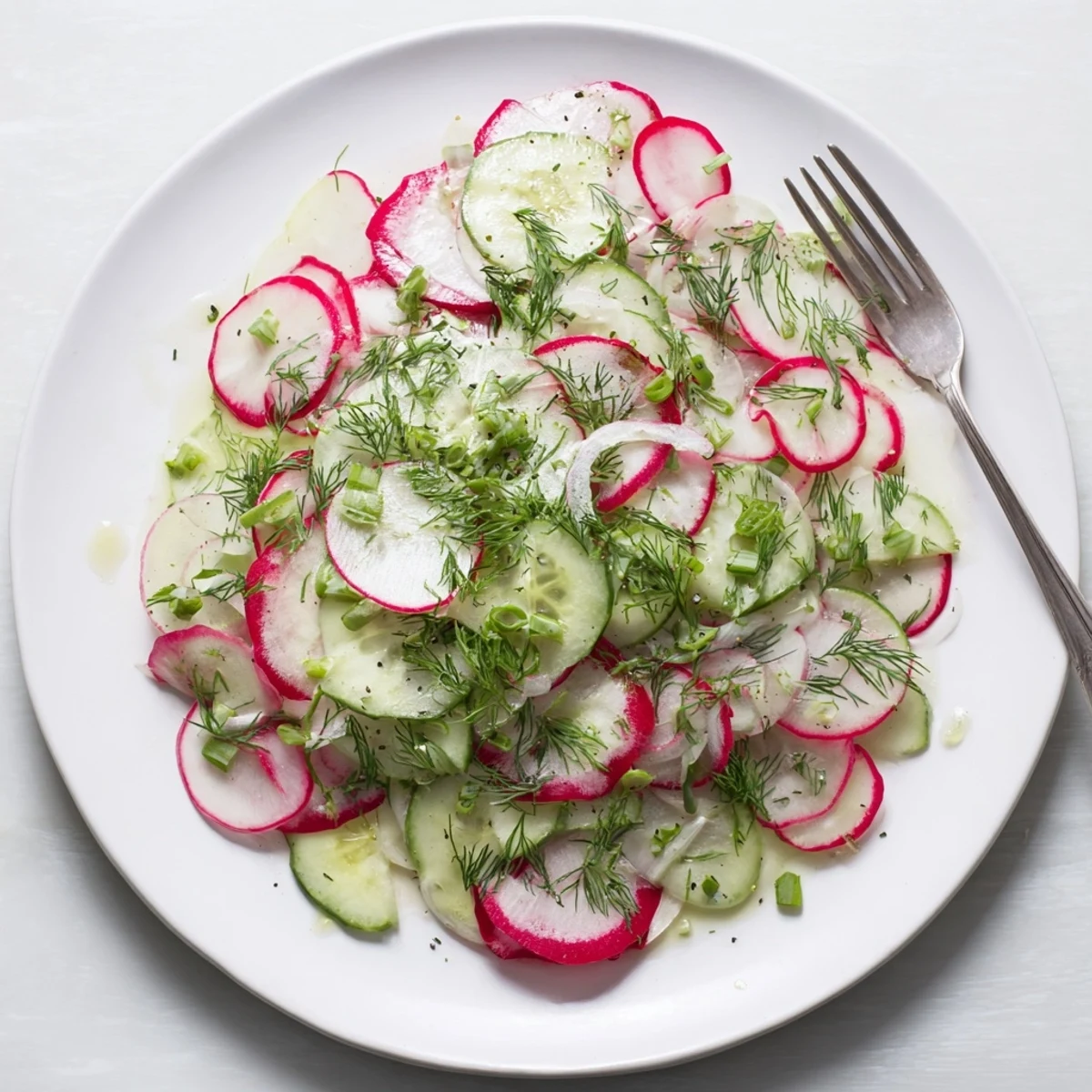 Fresh radish and cucumber salad arranged in a white serving bowl with vibrant green dill sprinkled on top