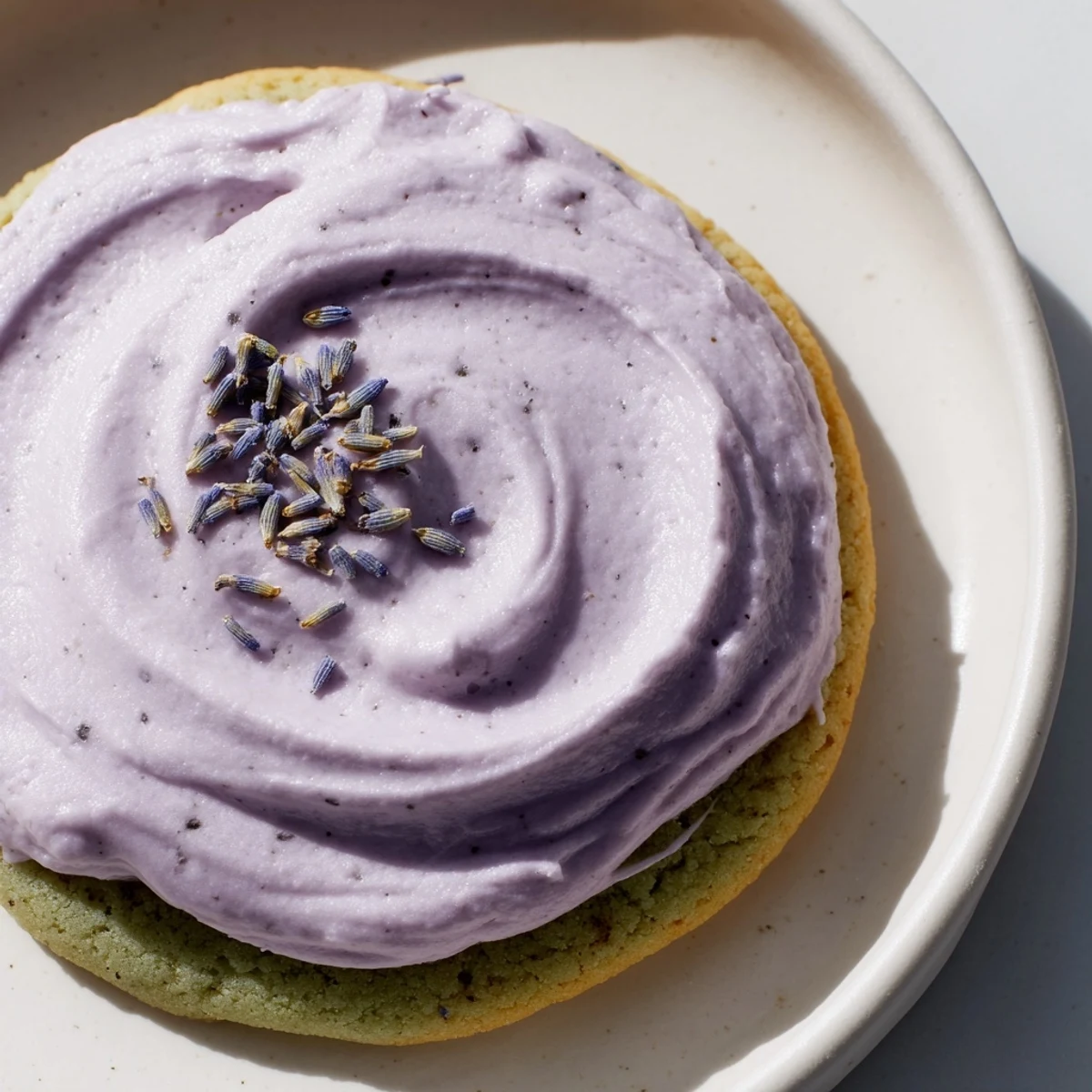 Soft green matcha sugar cookies topped with creamy lavender frosting on a rustic white plate