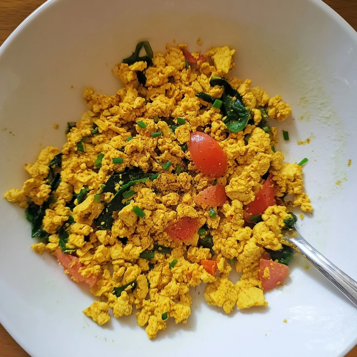 Tofu Scramble sizzling in skillet with turmeric, peppers, and wilted spinach.