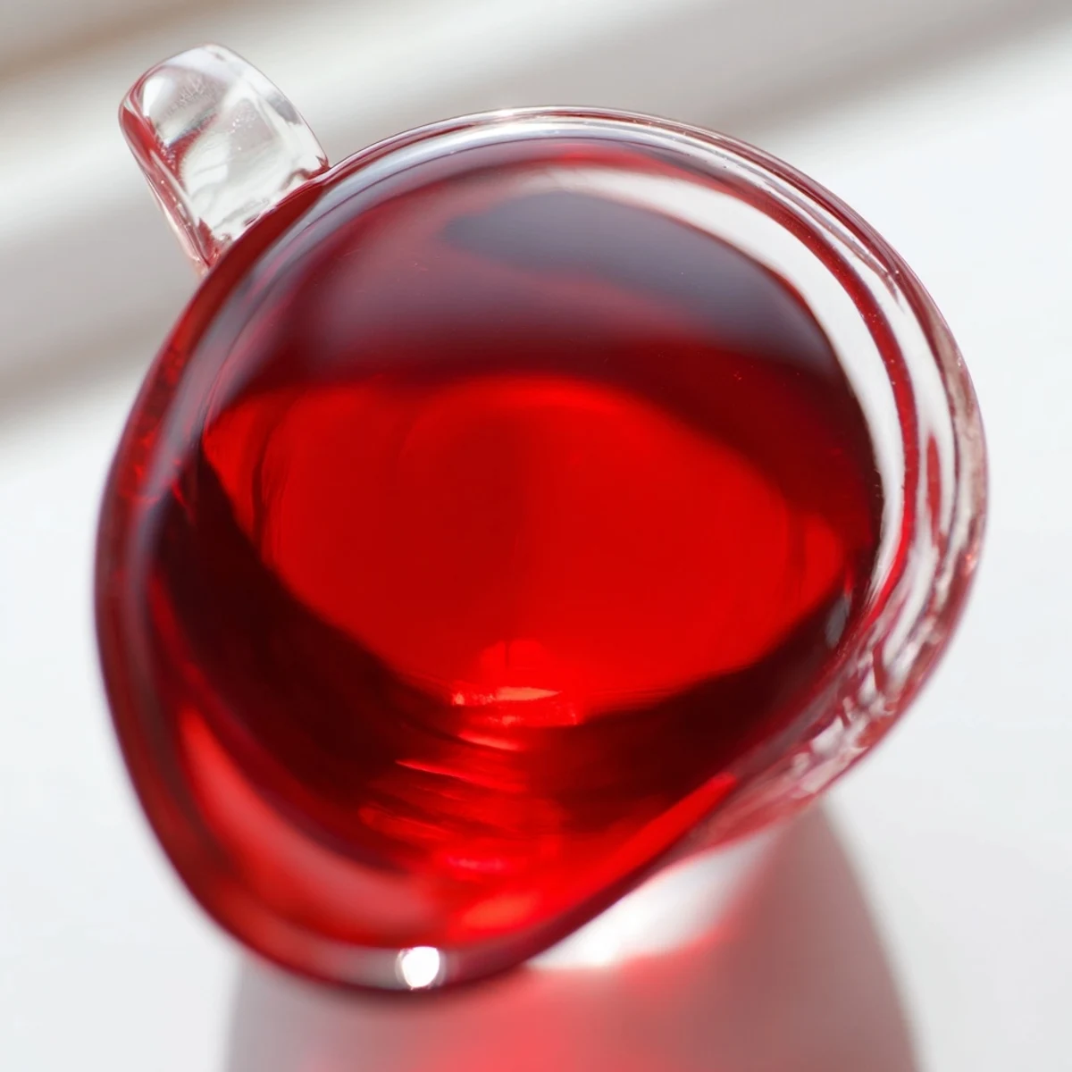 Homemade cranberry syrup poured into glass bottle showcasing vibrant deep red color and smooth texture
