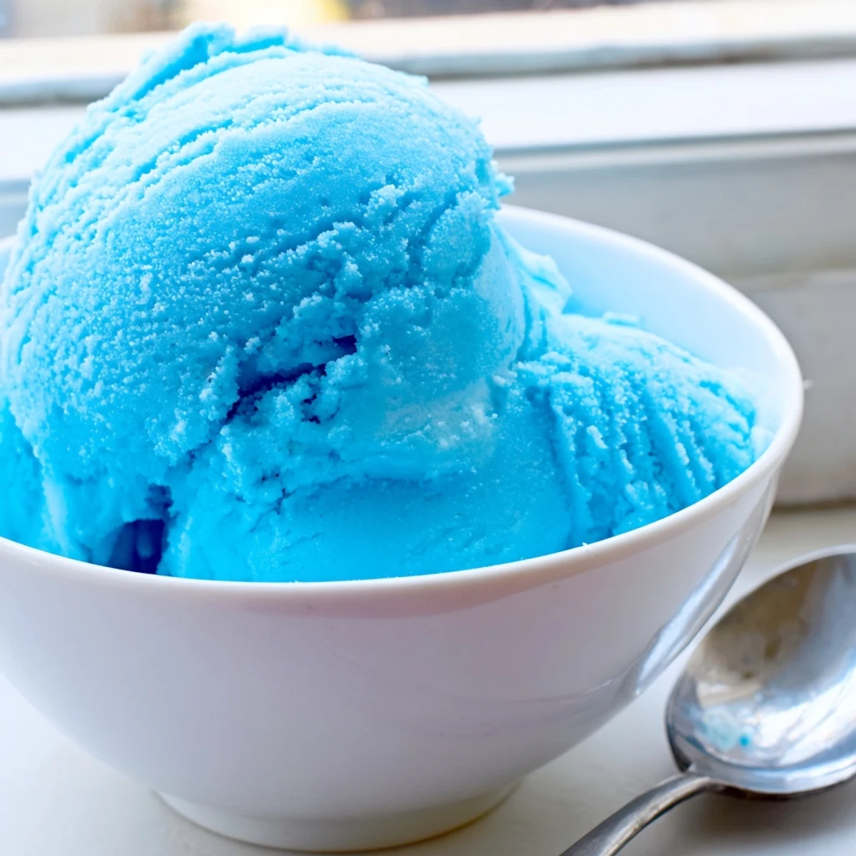 Smooth homemade blue moon ice cream with a bright sky-blue hue in a glass dish
