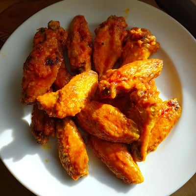 Freshly tossed hot Chicken Wings with Buffalo sauce, accompanied by crunchy carrot sticks on a rustic platter.