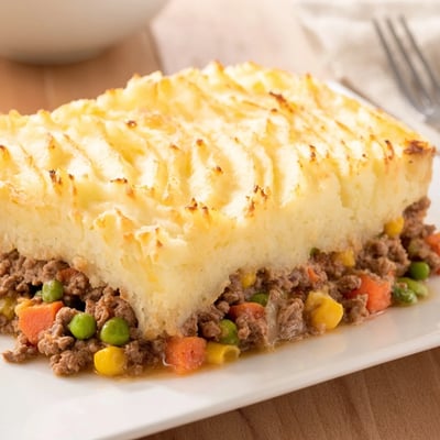 Golden baked Shepherds Pie with a fork marking the mashed potatoes, revealing savory beef and vegetable filling underneath, perfect for cozy family dinners.