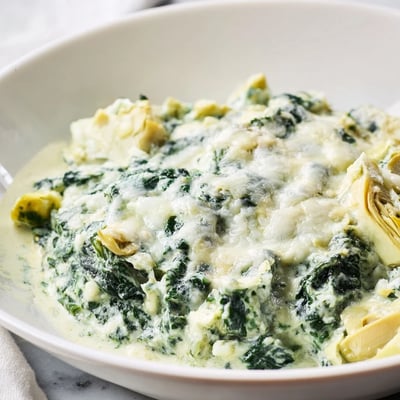 Homemade spinach dip with artichokes and melted cheese, bubbling golden top, perfect for parties and game day snacks.  